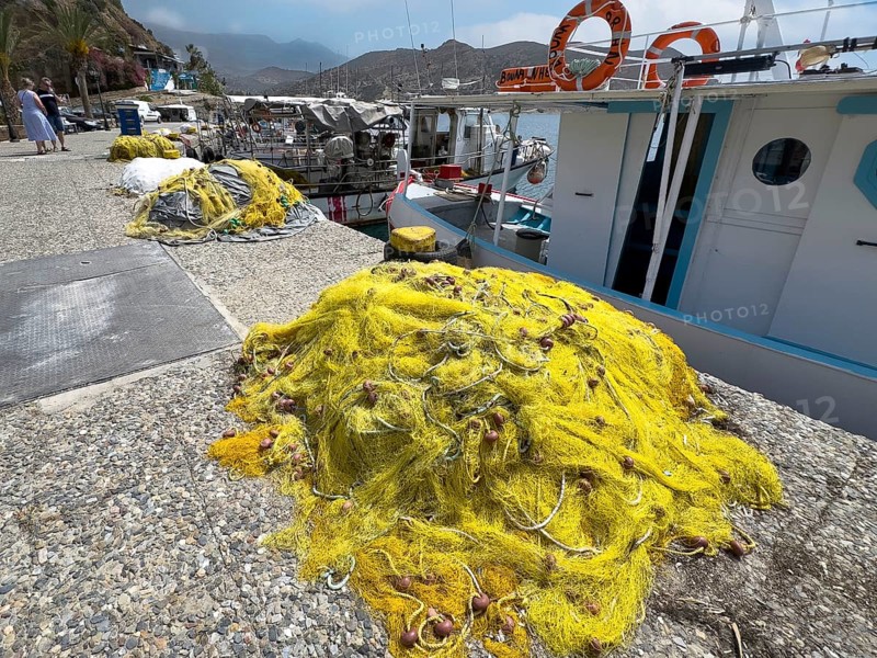Yellow fishing net lying on quay in front of fishing boat in small harbour of Agia Galini, Agia Galini, Crete, Greece, Europe