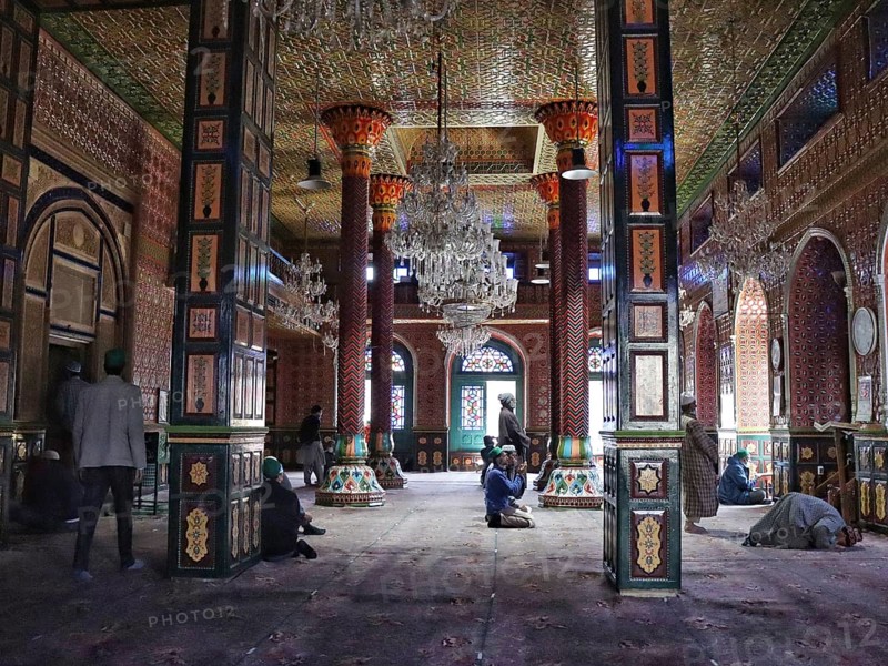 Ornate and colorful mosque interior with chandeliers, intricate designs on pillars, and people praying, Srinagar, Jammu and Kashmir, India, Asia