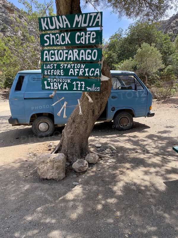 Tourist humorous funny sign on tree behind old Volkswagen VW Bus Bulli in front of entrance of Agiofarago Gorge Gorge of the Saints on south coast of island Crete with text Last Station in front of Africa, Libya 177 miles, Agiofarago Gorge, Crete, Greece, Europe