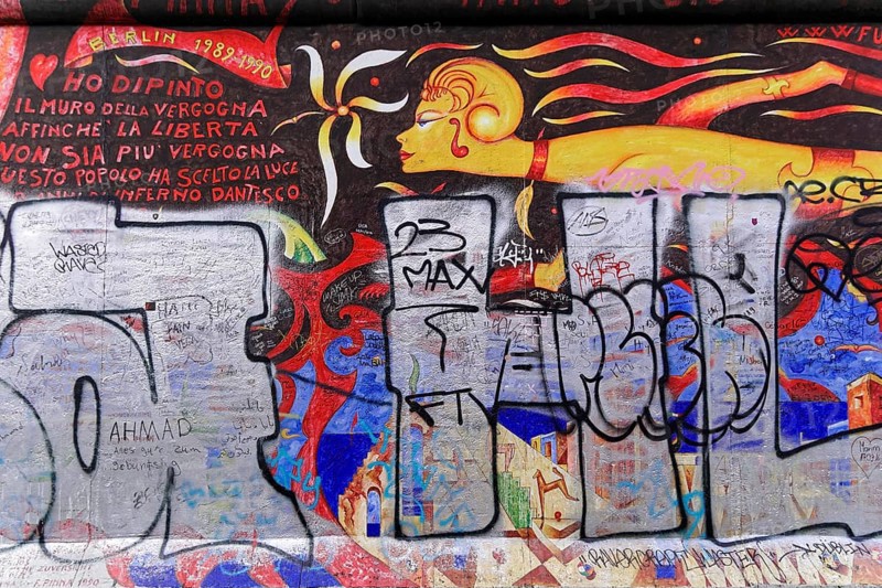 Colourful mural with a fiery female figure and Italian lettering, overlaid with large graffiti tags, mural, East Side Gallery, Mauergalerie, Berlin, Germany, Europe