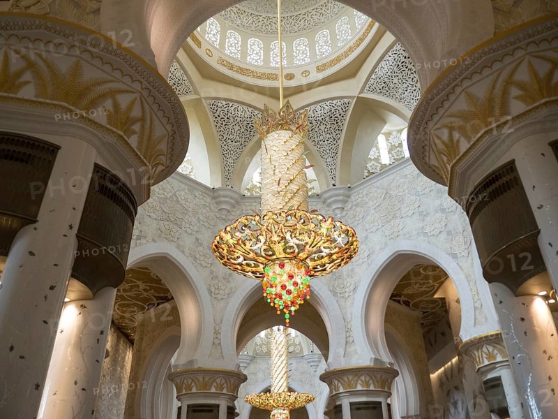 A sublime interior with an ornately decorated ceiling and a magnificent golden chandelier illuminating the room, gilded chandeliers in a mosque with white columns, Abu dhabi, arab emirates