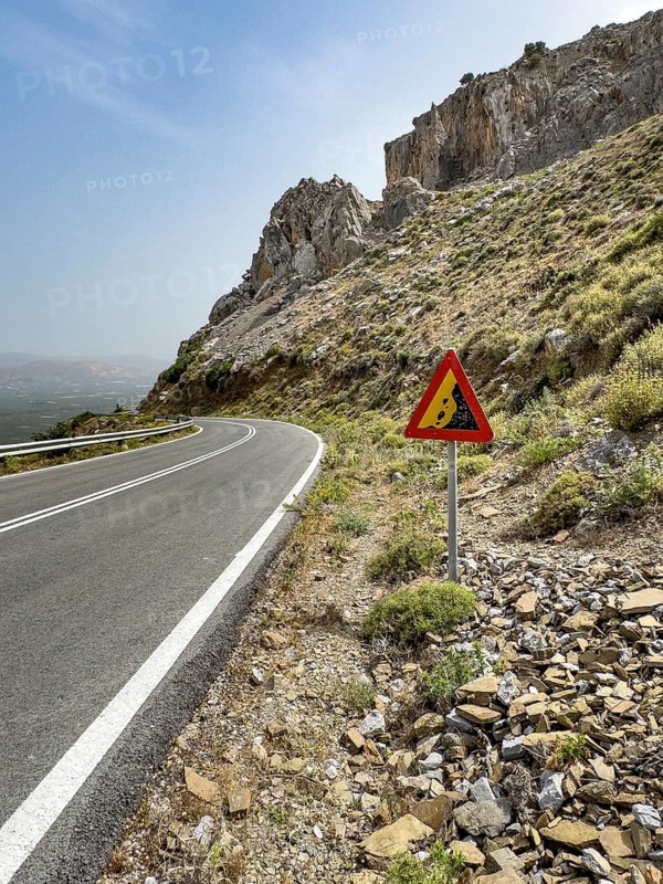 Warning sign for falling rocks next to mountain road near Plora in the background rocky mountains, Crete, Greece, Europe