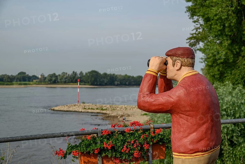 Man statue with binoculars on the riverside, flowers in the foreground and trees in the background, the rhine promenade of Rees with flowers and trees, Rees, Germany, Europe