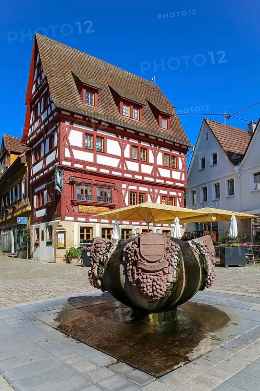 Fountain with inscription Gemmingen, stone grapes, water features, Ratsstueble restaurant at the back, traditionally a restaurant, pub, half-timbered house, three-storey half-timbered building with solid ground floor, gabled roof, ornamental half-timbering, bay windows, sunshades, Boennigheim, Ludwigsburg district, Baden-Wuerttemberg, Germany, Europe
