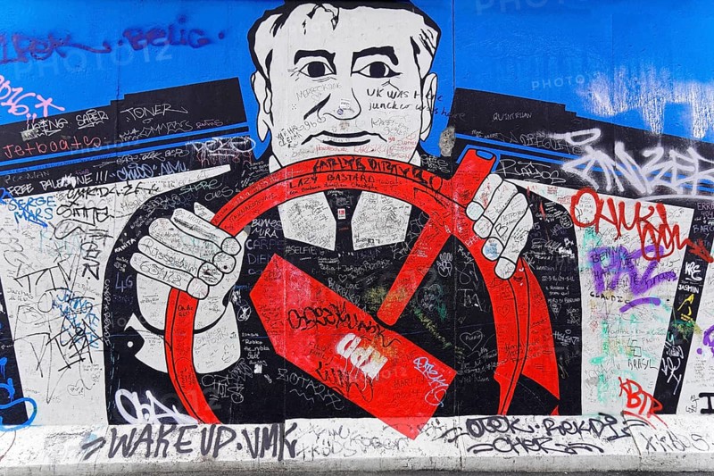 Mural shows a man with a steering wheel, police uniform, overlaid with numerous graffiti and scribbles, mural, East Side Gallery, Mauergalerie, Berlin, Germany, Europe