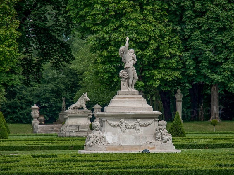 Elegant stone figure in a lush, well-kept garden surrounded by green trees and hedges, old red brick castle with towers and a large park with trees, plants and statues, Nordkirchen, Germany, Europe