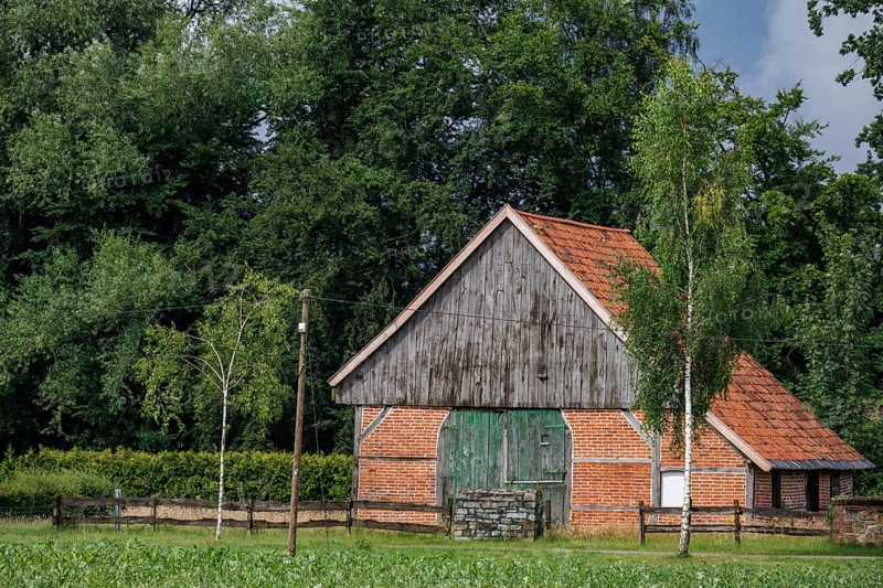 Old brick barn with a red roof, surrounded by trees and a green field on a summer day, Raesfeld, westphalia, germany