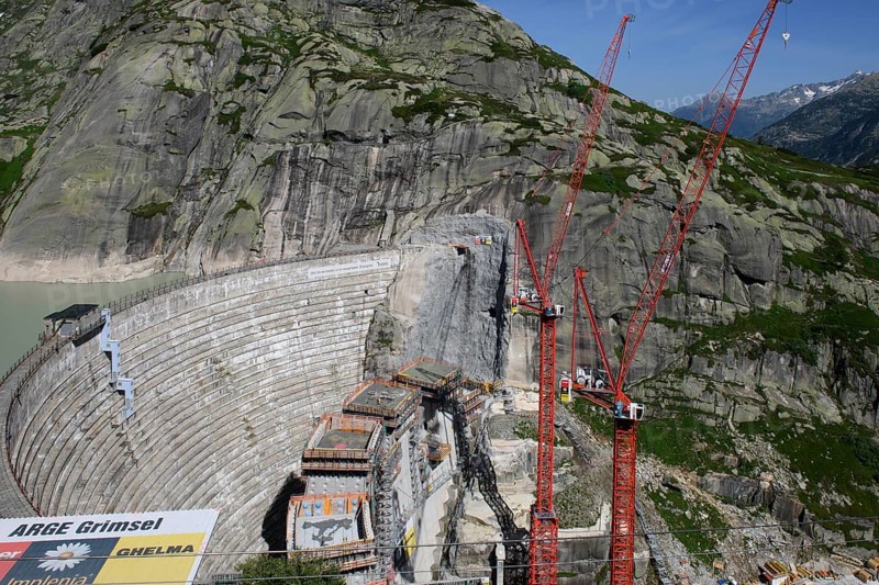 View of construction site of new dam for enlargement of reservoir Grimselsee replacement dam Spitallamm on the Grimsel in the Bernese Oberland, left old dam next to Grimsel Hospiz Grimselhospiz, right two large red cranes, Guttanen, Canton Bern, Switzerland, Europe