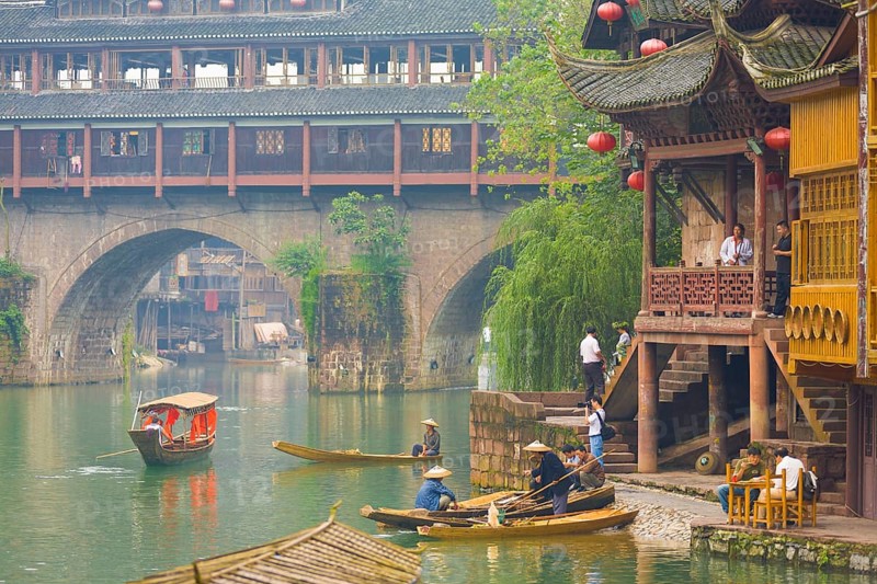 Fenghuang, China, September 10, 2007: Tourists and boats hang around riverside at the Phoenix Hong or Huangsi Bridge in the traditional Miao village of Fenghuang, Asia