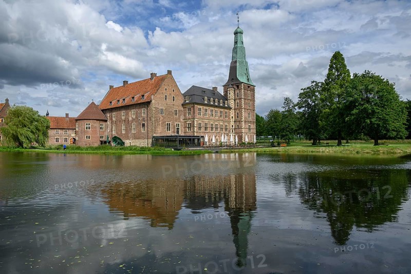 Large castle with brick walls and towers by a pond with reflections, surrounded by trees under a cloudy sky, Raesfeld, North Rhine-Westphalia, Germany, Europe