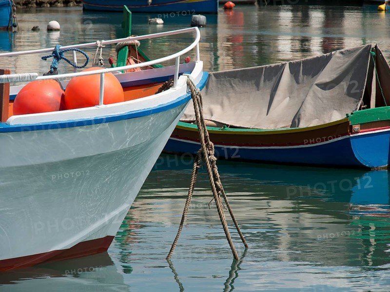 A quiet harbour with anchored boats floating on the reflecting water, marsaxlokk, mediterranean sea, malta
