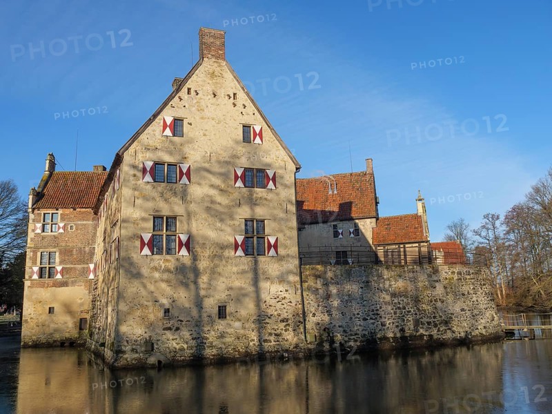 A historic moated castle with several windows and red shutters, on the banks of a pond, lüdinghausen, westphalia, germany