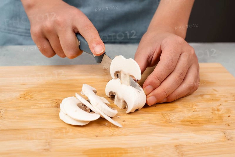 Cutting champignon mushrooms on a wooden board, prepare salad, healthy food with vegetables, fresh organic nutrition, cooking ingredients