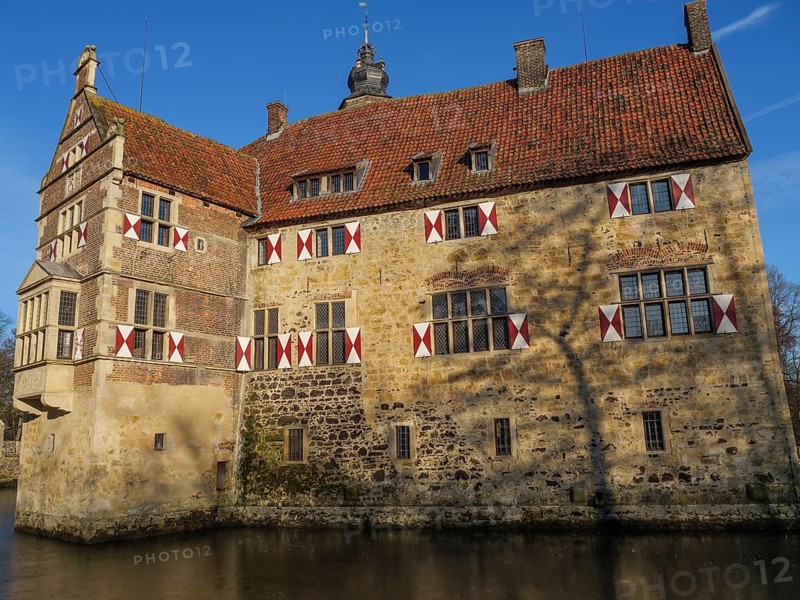 A moated castle with red and white shutters and a red roof, surrounded by water, lüdinghausen, westphalia, germany