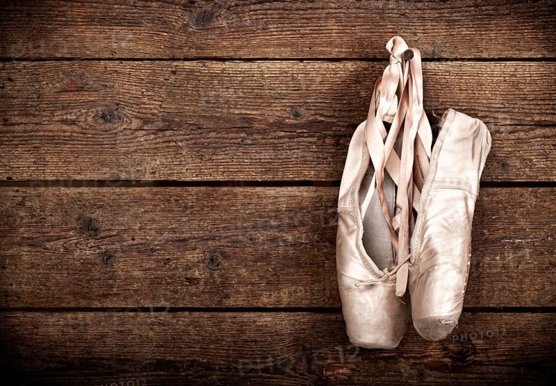 Old used pink ballet shoes hanging on wooden background