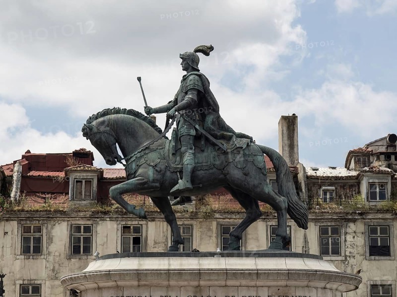 A statuesque equestrian figure in armour on a horse under a slightly cloudy sky in front of old buildings, Lisbon, portugal