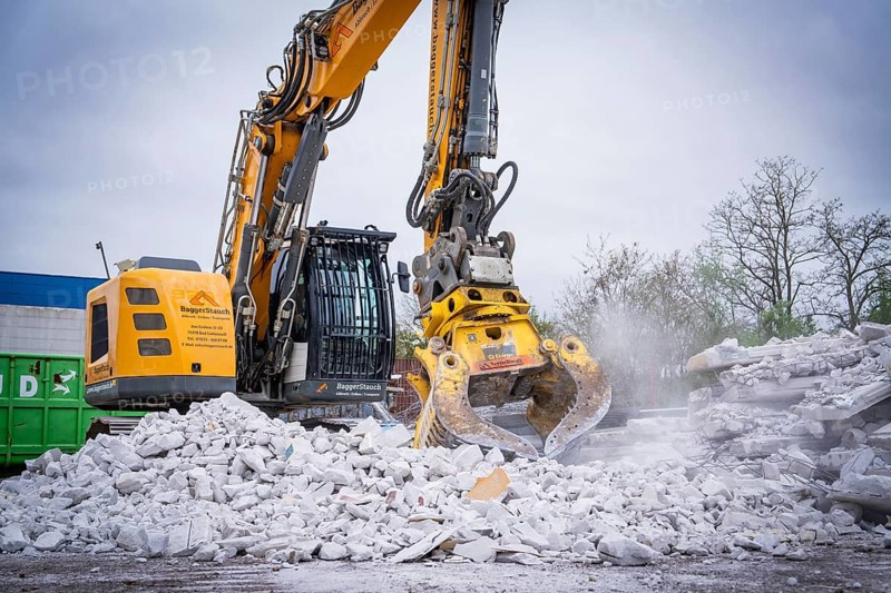 Large yellow excavator with metal grab shredding rubble on a construction site, trees in the background, demolition site, Saarbrücken, Germany, Europe