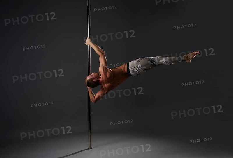 Image of strong gymnast exercising on pylon in studio