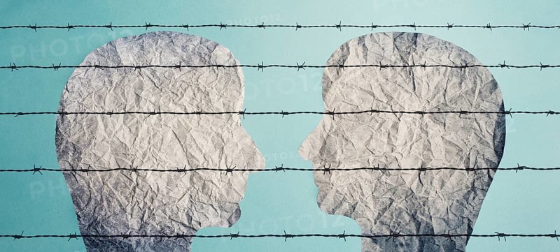 Two silhouettes of faces look at each other behind a barbed fence, refugee camp, prisoners