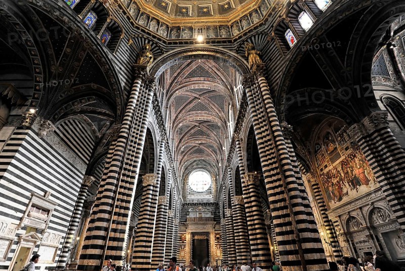 The central nave of the cathedral with its black and white striped marble columns, cross and round arches, Siena, Tuscany, Italy, Europe, Impressive interior of a cathedral with towering columns, Gothic architecture, decorations and people in attendance, Europe