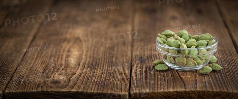Wasabi coated Peanuts as high detailed close-up shot on a vintage wooden table (selective focus)