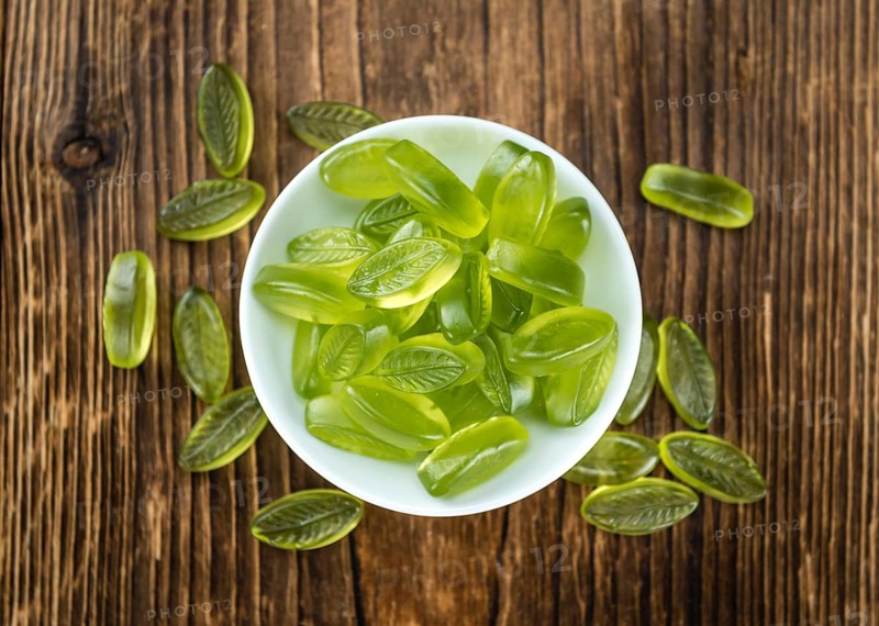 Heap of gummy candy with lime taste on wooden background (selective focus, close-up shot)