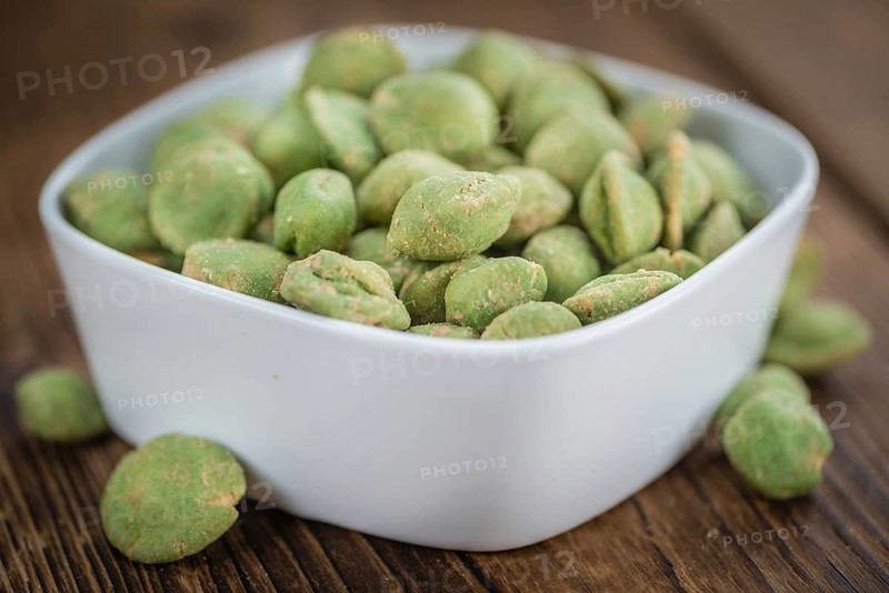 Wasabi coated Peanuts as high detailed close-up shot on a vintage wooden table (selective focus)