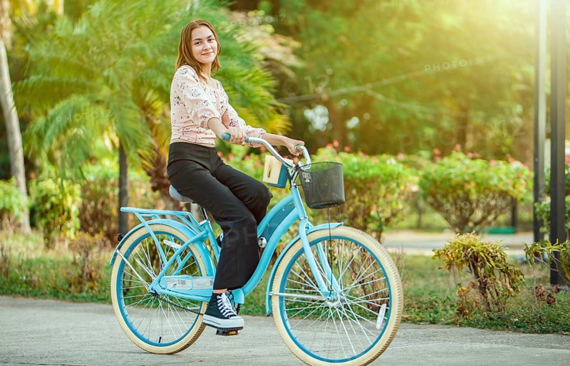 Portrait of beautiful smiling young woman riding a bicycle at sunset, looking at camera