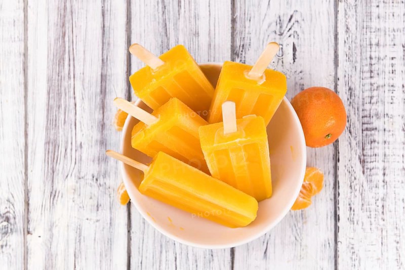 Homemade Tangerine Popsicles with some fresh fruits (close-up shot) on a vintage background