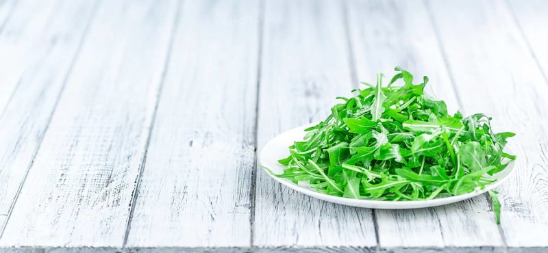 Wooden table with fresh Arugula as detailed close-up shot (selective focus)