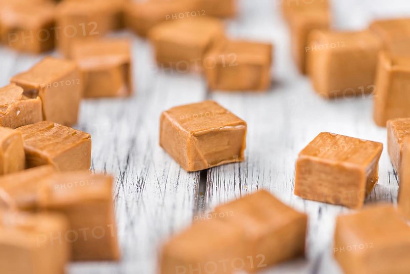 Caramel pieces as high detailed close-up shot on a vintage wooden table (selective focus)