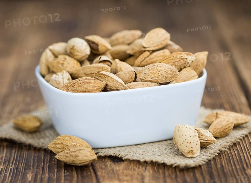 Roasted Almonds (in shell) on an old wooden table (close-up shot, selective focus)