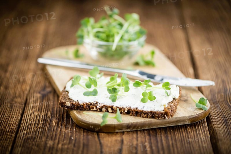 An old wooden table with healthy food (slice of bread, cream cheese and fresh cutted cress), selective focus