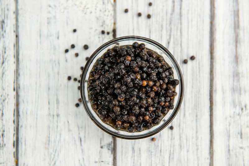 Preserved black Peppercorns on a wooden table as close-up shot