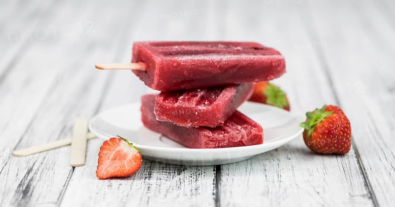 Old wooden table with homemade Strawberry Popsicles (close-up shot, selective focus)