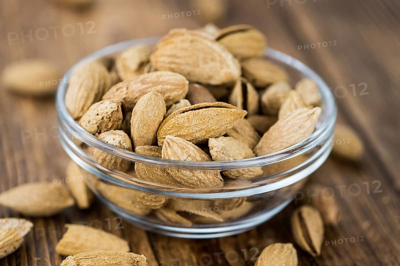 Roasted Almonds (in shell) on an old wooden table (close-up shot, selective focus)
