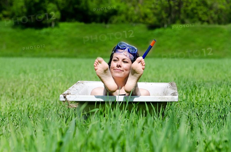 Happy Woman with a Diving Mask Lying in a Bathtub on the Green Field and Showing Her Feet in a Sunny Day in Ticino, Switzerland, Europe