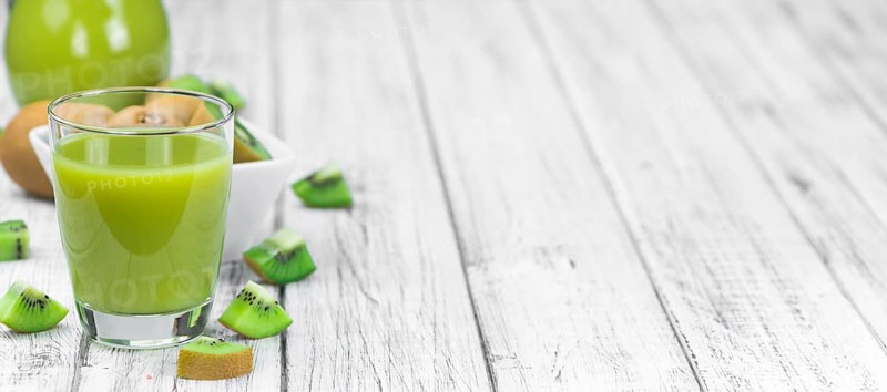 Wooden table with fresh made Kiwi Smoothie (close-up shot, selective focus)