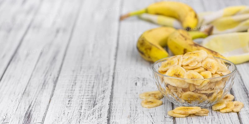 Homemade Dried Banana Chips on an wooden table as detailed close-up shot, selective focus