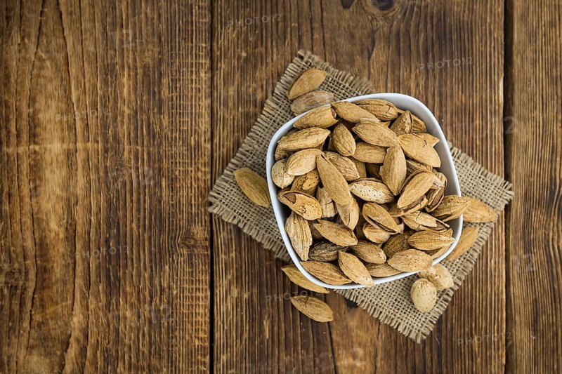 An old wooden table with roasted Almonds (in the shell) as detailed close-up shot (selective focus)