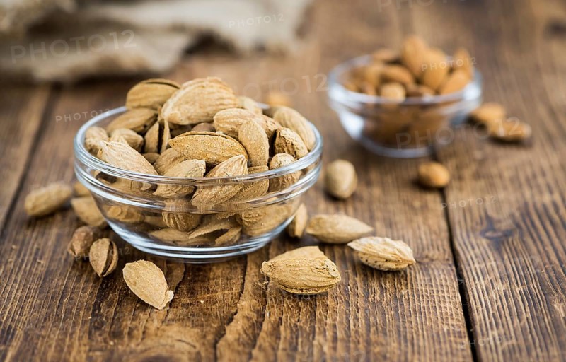 Roasted Almonds (in shell) on an old wooden table (close-up shot, selective focus)