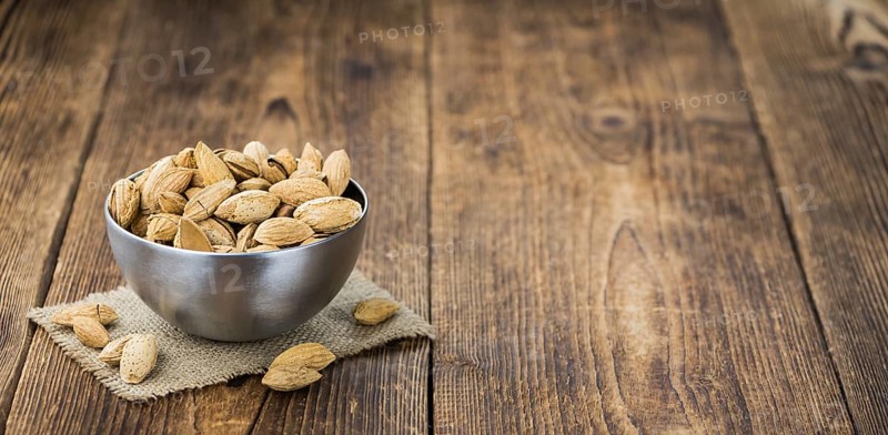 Roasted Almonds (in shell) on an old wooden table (close-up shot, selective focus)