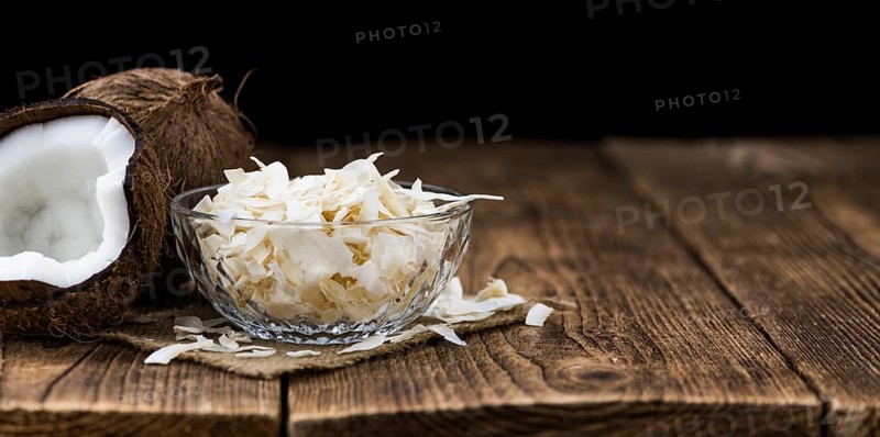 Healthy Coconut Flakes on a wooden table as detailed close-up shot (selective focus)