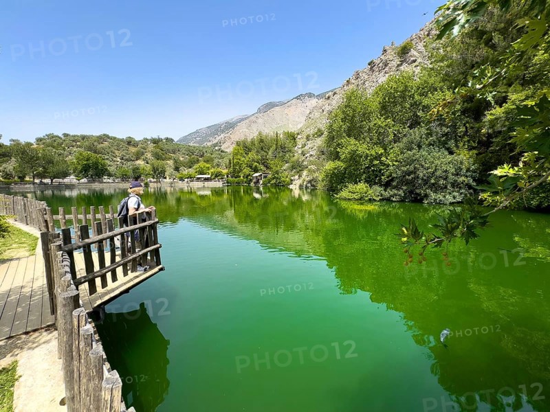 Tourist Holidaymaker standing on small viewing platform looking at artificial lake created in 1987 on the edge of the Psiloritis Mountains, fed by Votomos spring Votomos Lake Votomos Zaros Lake Zaros Lake Zaros Lake, in the background foothills of Psiloritis Mountains Psiloritis Massif Ida Mountains, Zaros, Crete, Greece, Europe