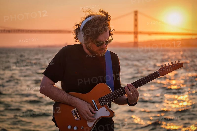 Hipster street musician in black playing electric guitar in street outdoors on sunset