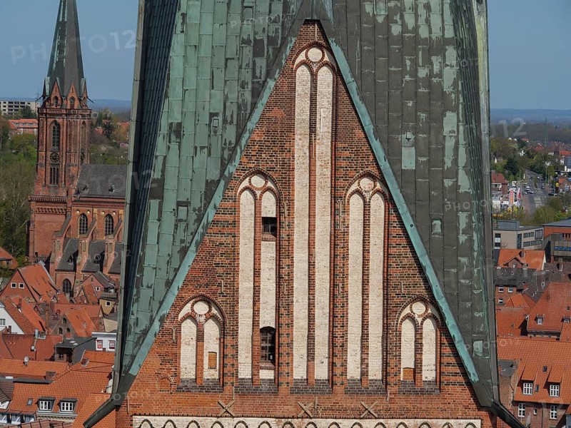 Close-up of a gothic brick church tower with neighbouring town houses, view over an old town with red roofs around imposing church towers, Lüneburg, Germany, Europe