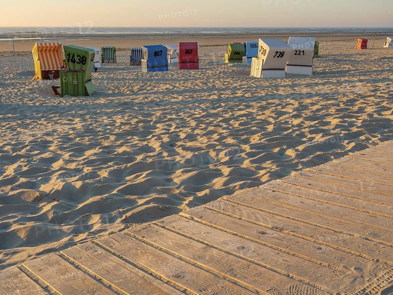 A wooden promenade leads past colourful beach chairs on the quiet sandy beach, langeoog, germany