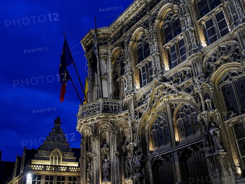 Monumental historic building with detailed facades and flags against a dramatic evening sky, Ghent, Belgium, Europe