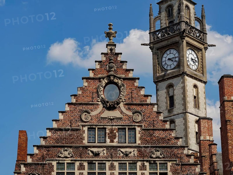 A striking clock tower and the gable of a brick house stand out against a blue sky, Ghent, Belgium, Europe
