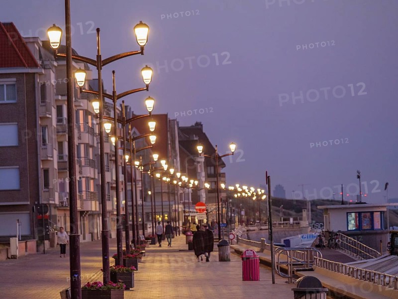 A promenade at dusk, illuminated by lanterns, people strolling along, quiet and peaceful atmosphere, DE Haan, Belgium, Europe